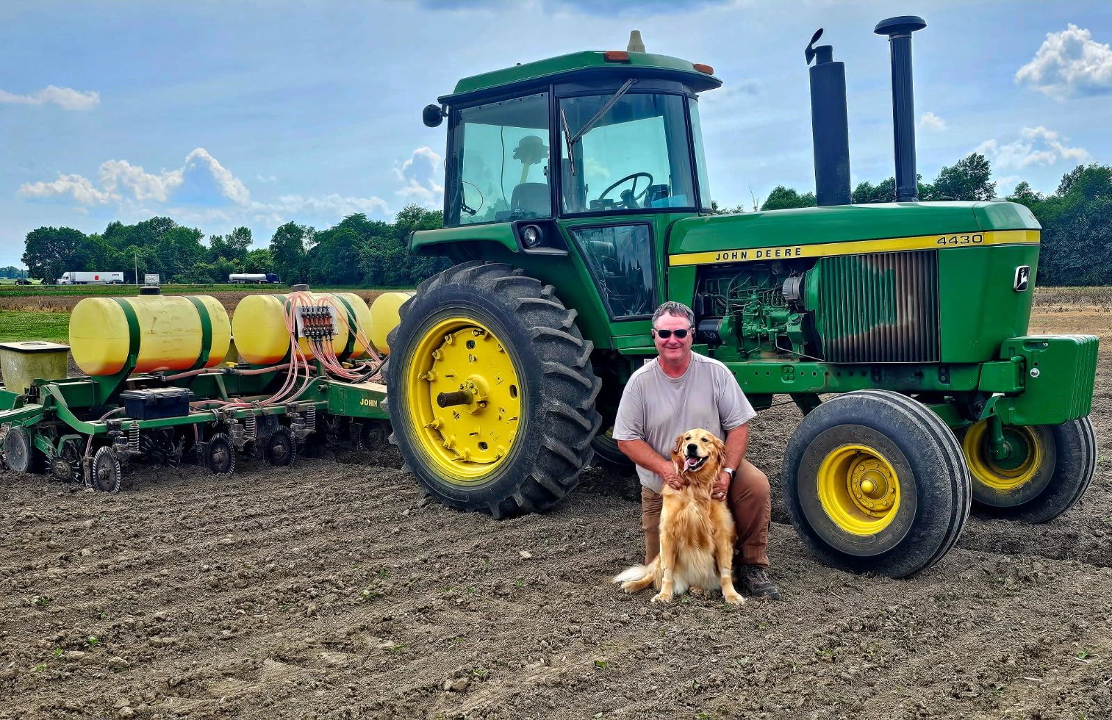 Mark Van Buren on his farm with his dog, Daisy Mae in front of John Deere tractor